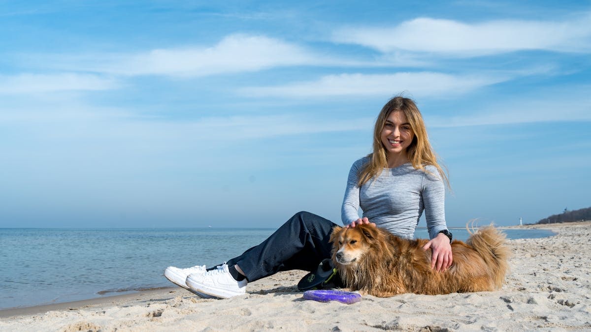 Woman enjoying a sunny day on Kołobrzeg beach with her dog, capturing the essence of leisure and companionship.